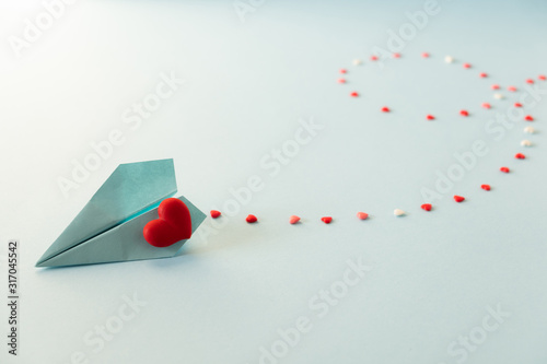 Valentine's Day background. Single blue paper plane with red heart on a pastel blue background.