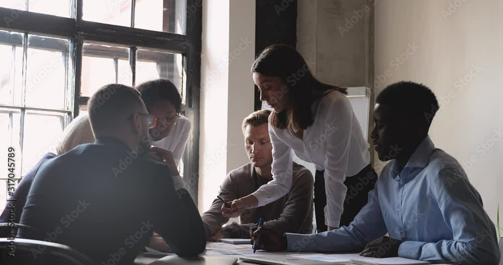 Serious female manager and diverse team analyze paperwork at meeting