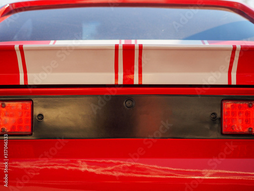 Old retro vintage red american muscle car with two white stripes rear view close up background
