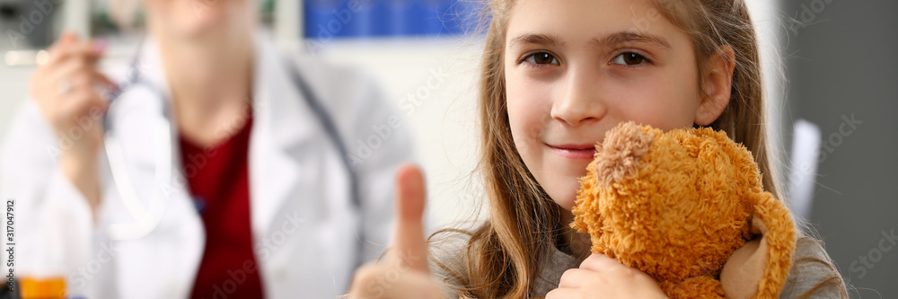 Happy little child girl hold teddy bear and thumbs up in hospital female excel doctor office. Happy little child girl hold teddy bear and thumbs up in hospital female excel doctor office.