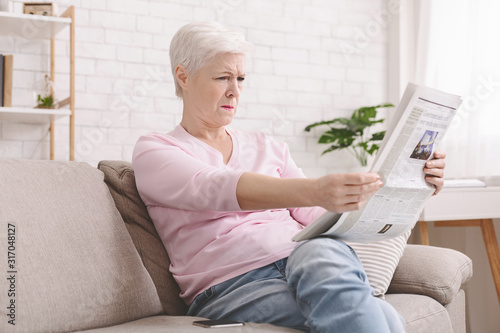 Senior lady squinting and holding newspaper far from eyes photo