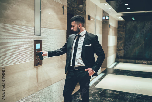 Executive man with takeaway coffee pressing elevator button