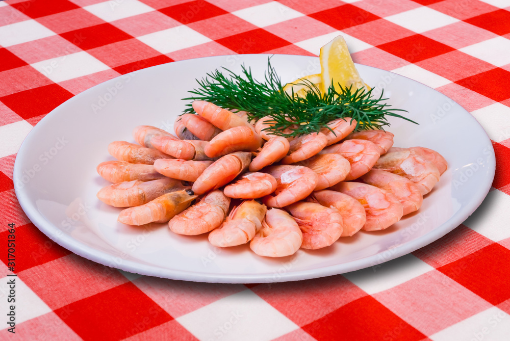 Plateful of cooked shrimps with lemon slice on checked tablecloth Plateful of cooked shrimps with lemon slice on checked tablecloth