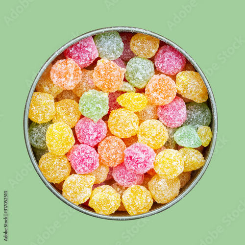 colorful multicolored sucking sweets Montpensier lollipops in a round tin box isolated on a green background close-up top view flat lay