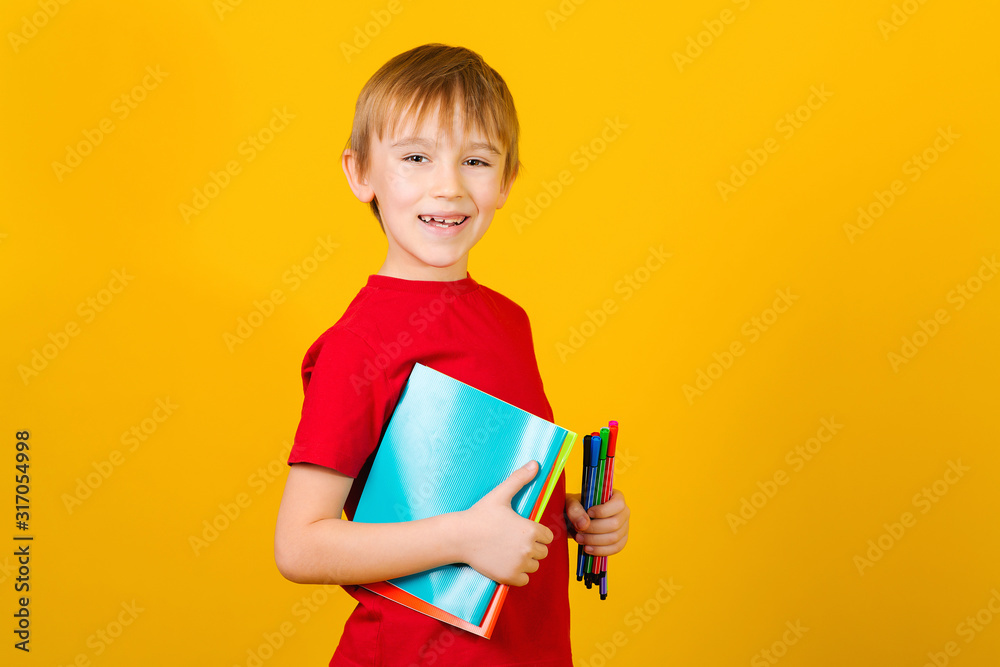 Happy boy holding school supplies over yellow background. Kid with notebooks and pens. Back to school concept Happy boy holding school supplies over yellow background. Kid with notebooks and pens. Back to school concept