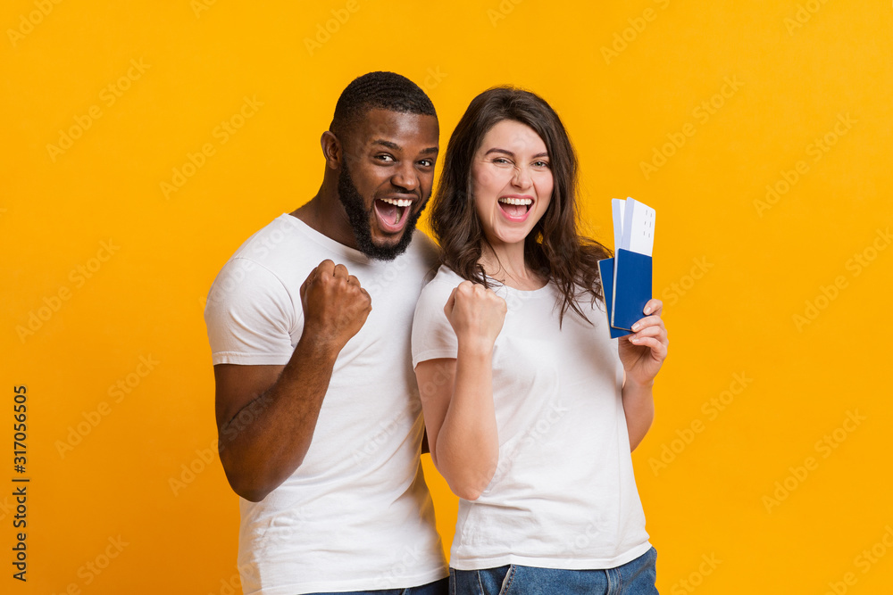 Overjoyed interracial couple holding passports with flying tickets, celebrating getting visa - obrazy, fototapety, plakaty 