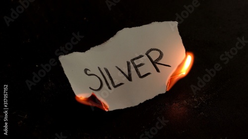 Silver word written on white paper burns. Fire with smoke and ashes on black background photo