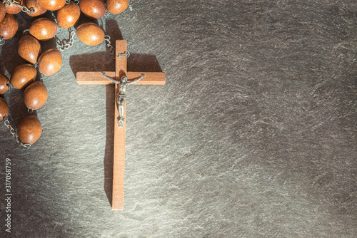 Old wooden Franciscan rosary, on the large Christian cross Jesus, a ray of sunshine illuminates the rosary on a gray stone background, religious and faith concept. photo