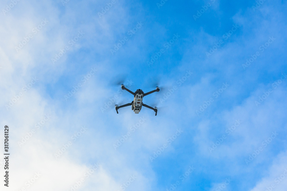 Small gray drone flying in the sky, quadcopter on a cloudy sky background.