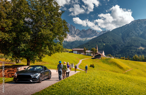 Awesome alpine highlands in sunny day. Breathtaking view of Church of Santa Maddalena. luxury car and hikers on road, is one of the most popular photo spot of Dolomite. Famous World place photo