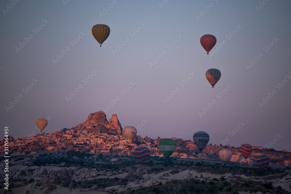 Cappadocia, Turkey: aerial view of Uchisar, ancient town of the historical region in Central Anatolia rich of exceptional natural wonders, with hot air balloons floating in the pink sky at dawn 