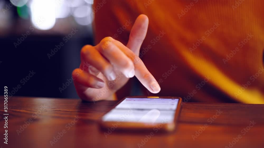 Phone - closeup female hand scrolling using app on smart phone in caffee. Closeup of hand using smartphone indoorsdoors. Mobile cell phone close up.