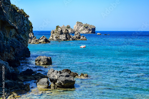 Fototapeta Naklejka Na Ścianę i Meble -  Paleokastritsa / Corfu, Greece: Ampelaki beach, clear turquoise water in a bay on the Adriatic Sea, cliffs, empty boat, in the summer afternoon.