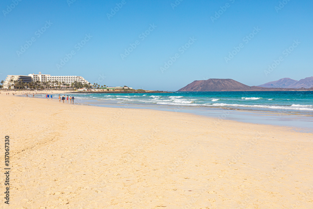 Beach hotel on Fuerteventura canary islands with the beach in front and the sea with blue azure aquamarine turquoise colors and a vulcano in the background blue sky