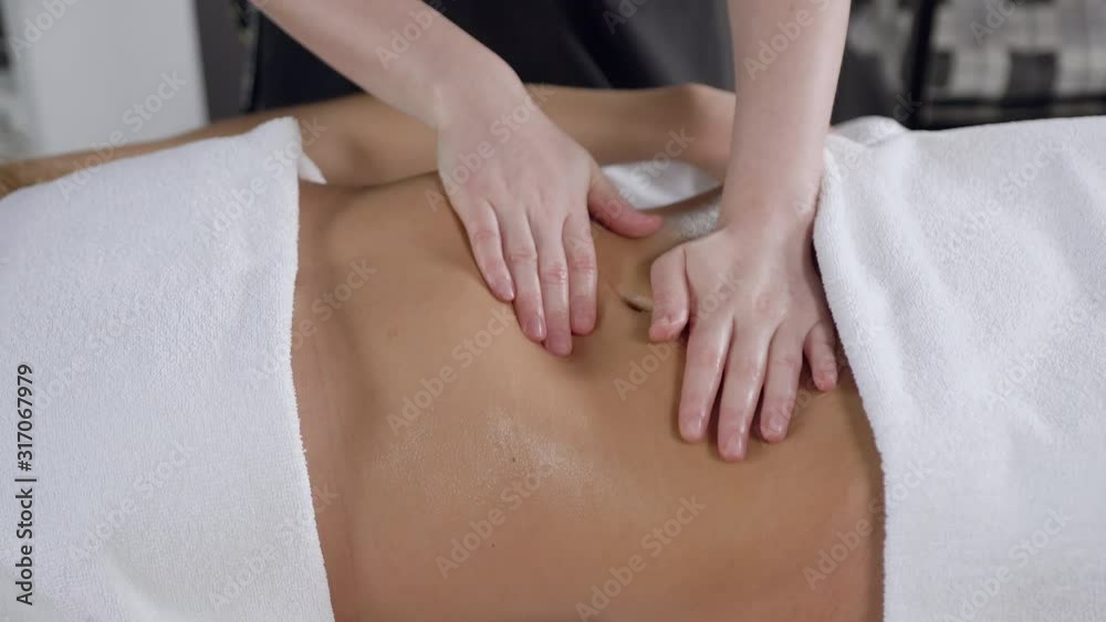 Side view of female specialist hands making stomach anti cellulite massage for smoothing stretch marks for woman client in spa salon Side view of female specialist hands making stomach anti cellulite massage for smoothing stretch marks for woman client in spa salon