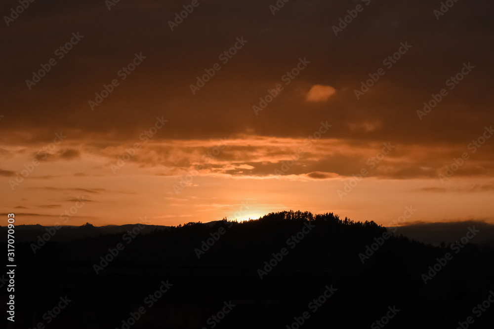 Beautiful orange sunset, the sun is hidden behind the mountains and trees