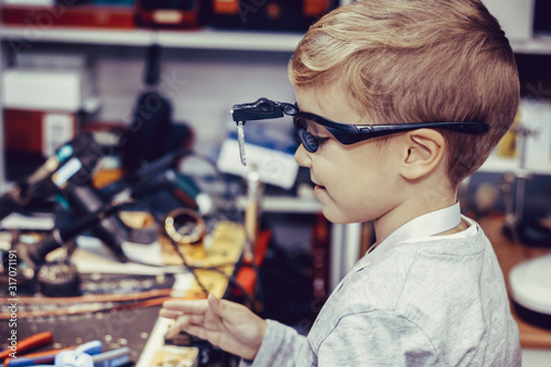 Small boy with magnifying eyeglasses in a workshop.