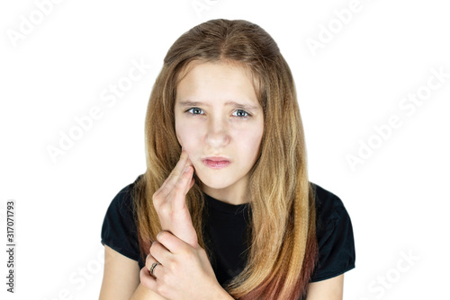 Sad young girl with blond hair on a white background holds her cheek and suffers from toothache. Medical concept