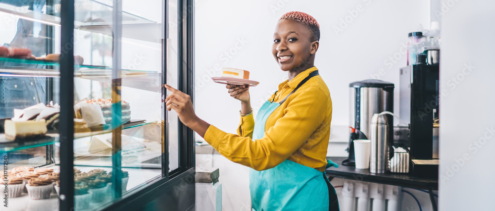 Shop assistant pointing at cake in pastry shop - obrazy, fototapety, plakaty 