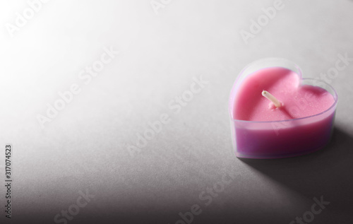 A heart-shaped pink candle on a gray discolored background. Sadness  melancholy from parting. The loneliness of a person. Selective focus.