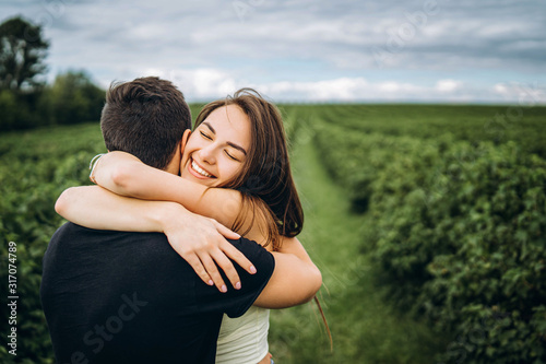 Cute young girl with long hair hugs her lover, smiling and with her eyes closed. Young couple walking in a field in nature © bedya