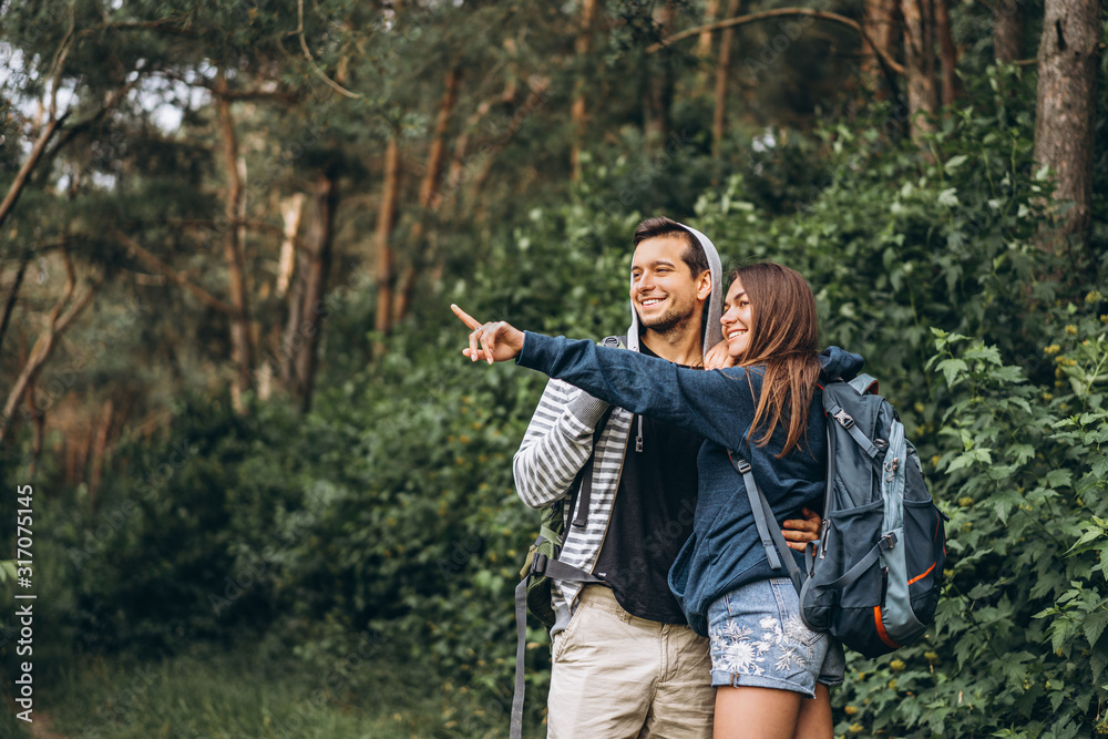 Young couple with backpacks on their backs smiling and walking in the forest, enjoy the walk Young couple with backpacks on their backs smiling and walking in the forest, enjoy the walk