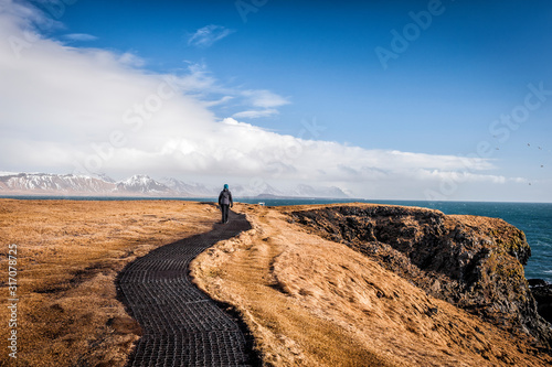 Tourist walking on Hellnar-Arnarstapi coastal path, Snaefellsnes peninsula (region of Vesturland, Iceland) photo