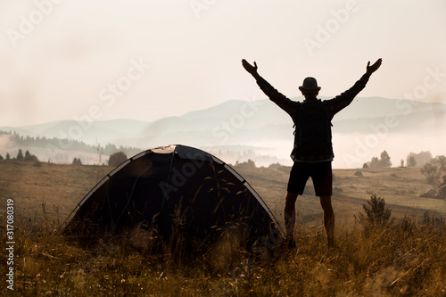 Silhouette of man raised his hands with the backpack on camping holidays at sunset