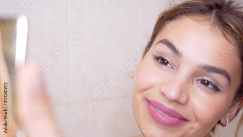 Confident happy young woman applying make up on eyeleashes, getting ready in the morning, smiling beautiful girl doing make up put cosmetics on face looking in mirror in bathroom at home