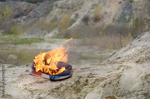 Burning sports sneakers or gym shoes on fire stand on sandy beach coast. Athlete burned out. Physical exertion during training concept photo