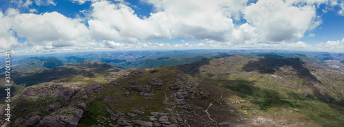 Aerial super wide panorama of the Itacolomi mountain top ridge from above the characteristic peak in Ouro Preto, Brazil, against a blue sky with clouds