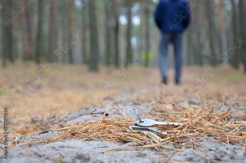 Young man loses his keys bunch on Russian autumn fir wood path. Carelessness and losing keys concept photo