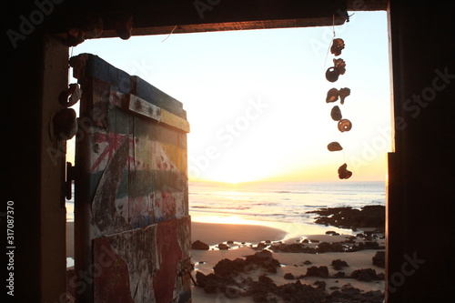 old, open door leads to the beach, sun is shining in, artistic drawings and shell neckless