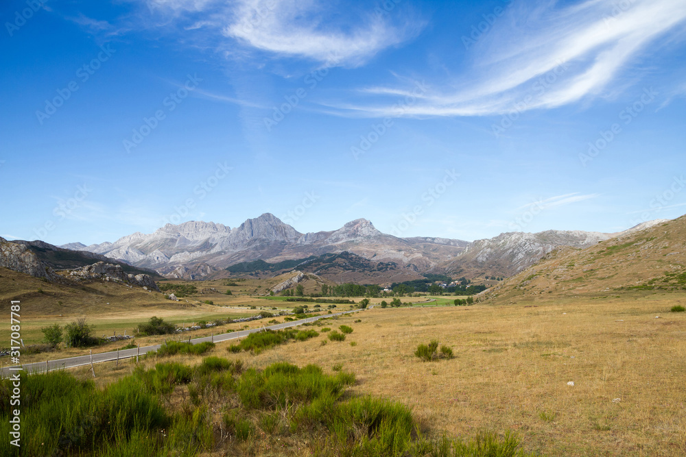 Vista de paisaje veraniego con carretera de acceso al pueblo de San Emiliano  en un valle rodeado con altas montañas. León. España