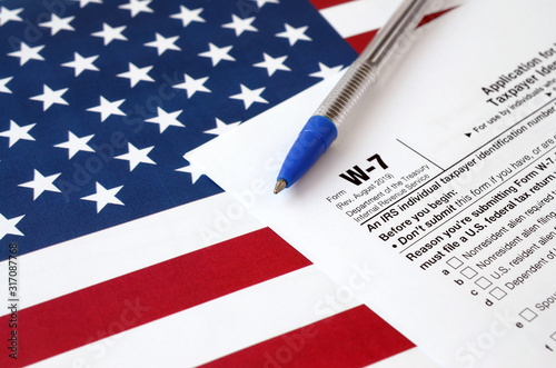 Form W-7 Application for IRS Individual taxpayer identification number and blue pen on United States flag. Internal revenue service tax form