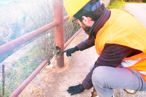 Ingegnere chimico sta valutando i danni della corrosione generalizzata sulla ringhiera di un ponte