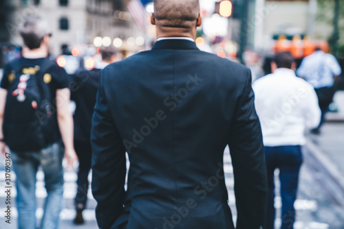 Bald ethnic male employee in suit crossing road