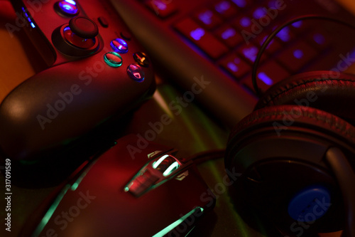 Modern gamepad and gaming mouse lies with keyboard and headphones on table in dark playroom scene. Computer game competition concept photo