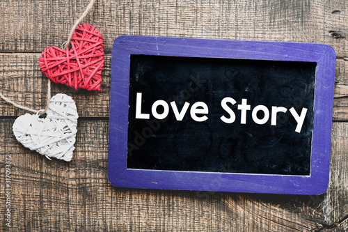 Love story text written on chalk board and wooden background, red and white heart on wood.