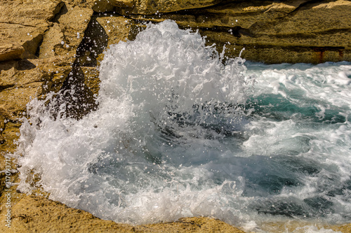 Turquoise wave breaks on rocks of the Sliema coast, Malta. Wave and splashes on rocky Malta beach.