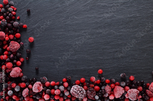 Frozen berries fruits in the bottom left cornern on slate slab. Mix of raspberries, blueberries. and red currants. Top view. Copyspace. photo