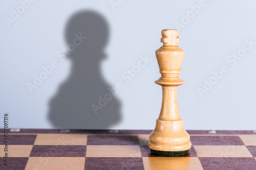 White chess king with pawn shadow. Exaggeration of possibilities concept. photo