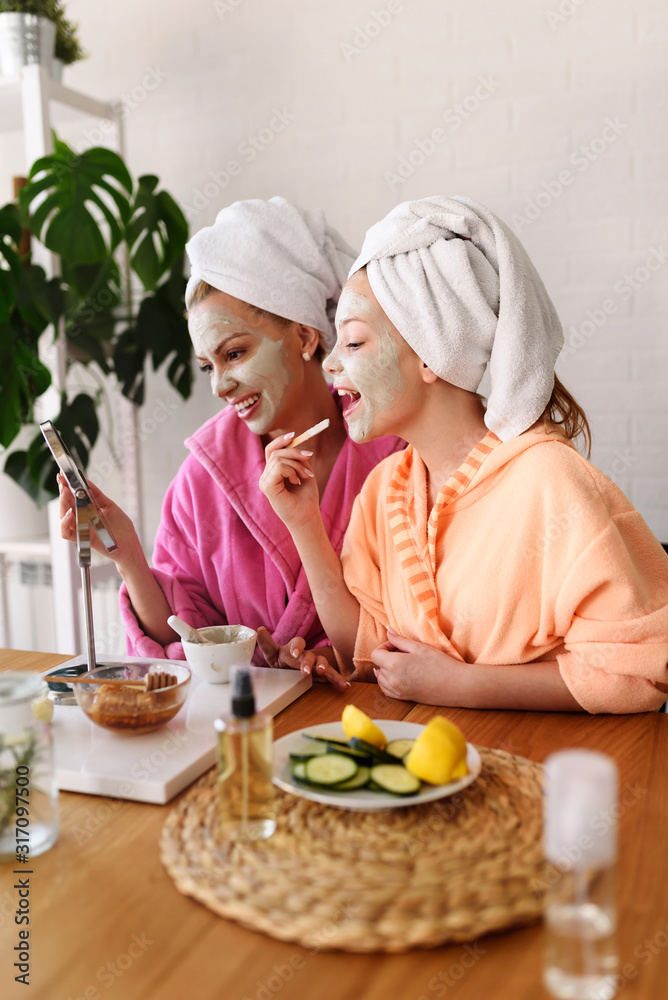 Mother and daughter in bathrobes and towels on head using natural cosmetics and having fun together at home Mother and daughter in bathrobes and towels on head using natural cosmetics and having fun together at home