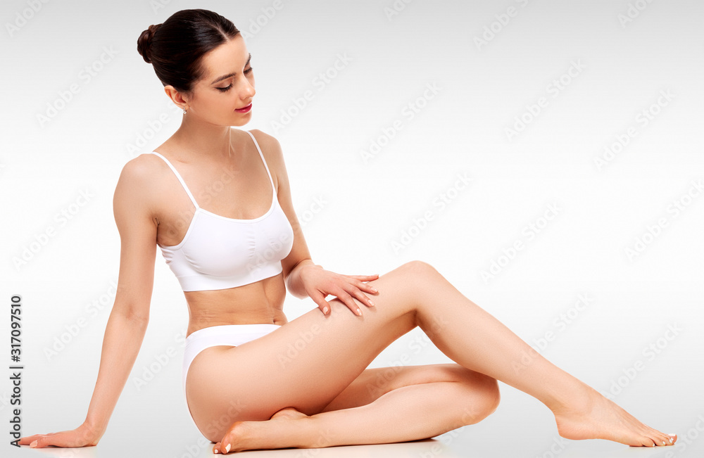 Wellness and beauty concept, beautiful slim woman in white underwear sitting on a floor against a grey background with copyspace