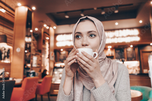 Muslim woman drinks coffee in a cafe at a table