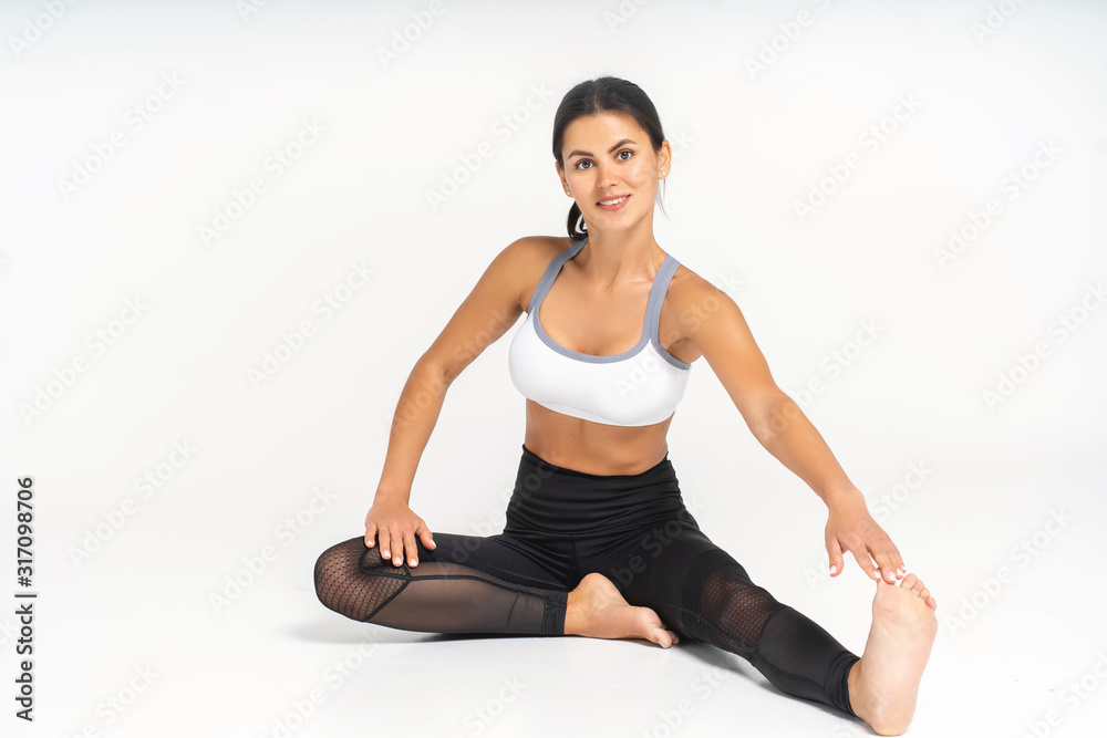 Dedicated to fitness. Front view of beautiful young woman in sportswear doing stretching while sitting on the floor at white studio