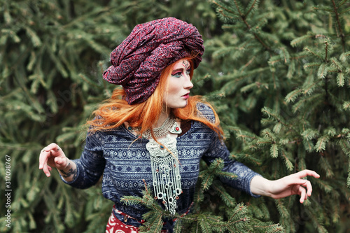 Extravagant redhead woman in ethnic national dress dancing or posing in a mistical forest