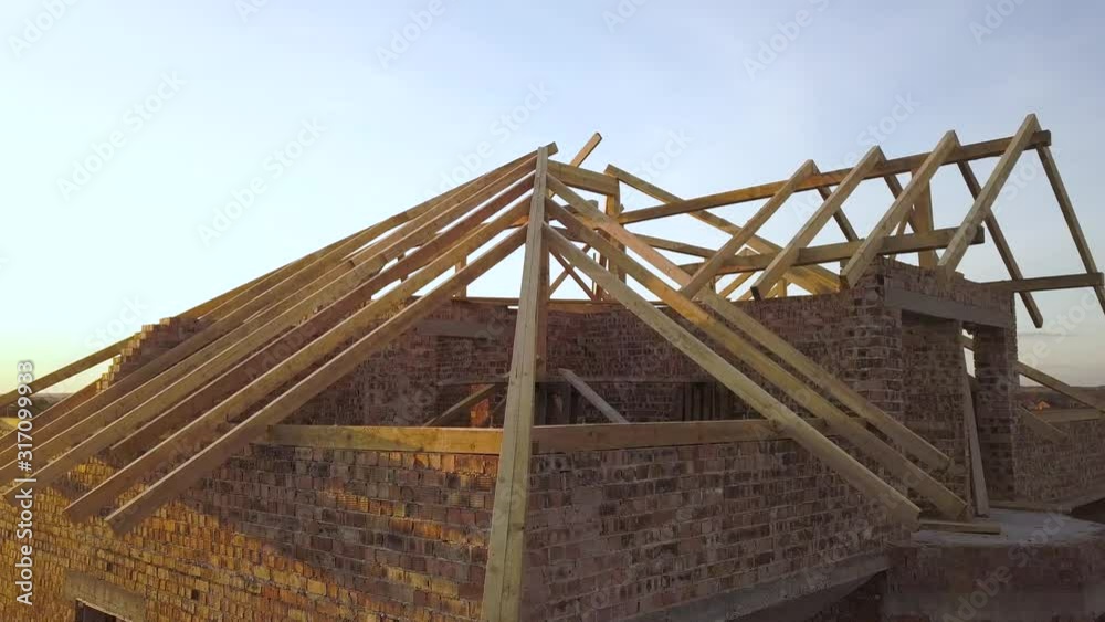 Aerial view of unfinished brick house with wooden roof structure under construction. Aerial view of unfinished brick house with wooden roof structure under construction.