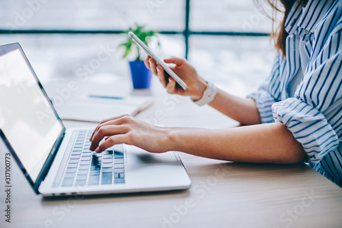 Anonymous woman in casual clothing working with blank screen laptop and smartphone at office