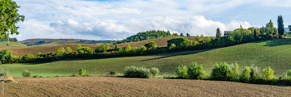 Beautiful landscape in Tuscany - wave hills covered green grass with cloudy sky. Tuscany, Italy, Europe. Wide banner.